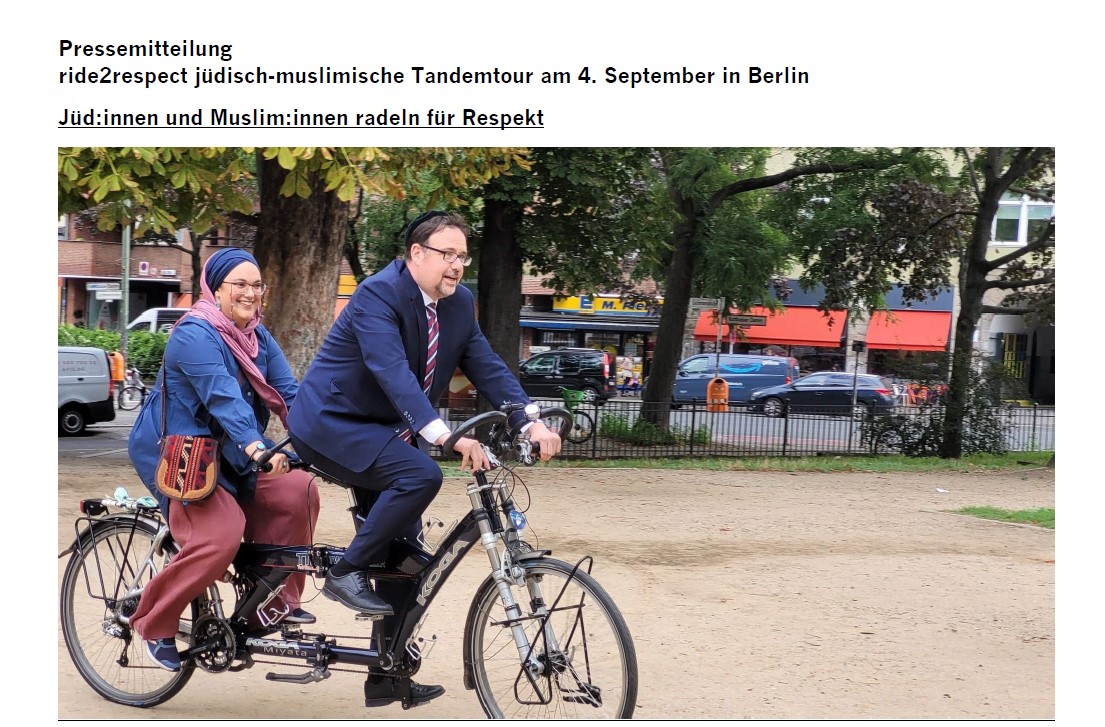 Teilansicht einer Pressemitteilung mit sichtbarem Foto, auf dem eine Frau mit Kopftuch und ein Mann mit Kippa gemeinsam auf einem Tandemrad fahren.